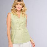 Woman with blonde wavy wig wearing a light green sleeveless top.