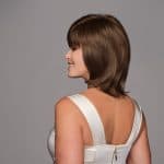 Woman with short brown wig, side profile, smiling, against gray background.