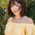 Woman with short wavy brown wig outdoors, yellow off-shoulder top.