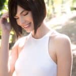 Woman with short brown bob wig outdoors, smiling and touching her hair.