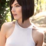 Woman with short, dark brown bob wig outdoors in sunlight.