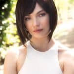 Woman with short, dark brown bob wig outdoors in sunlight.
