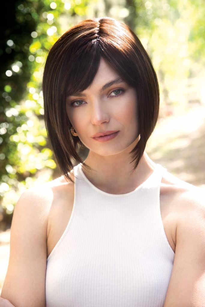 Woman with short, dark brown bob wig outdoors in sunlight.
