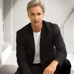Man with styled gray wig in black blazer and white shirt.
