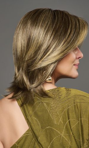 Side view of a woman with a layered blonde wig and a green top.