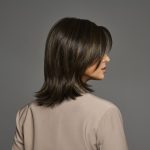 Side view of a woman with a layered brown wig and straight hair.