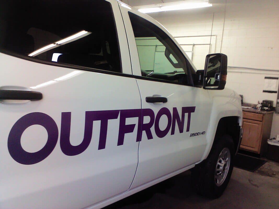 White vehicle with Outfront logo and handicap sign decal on door.