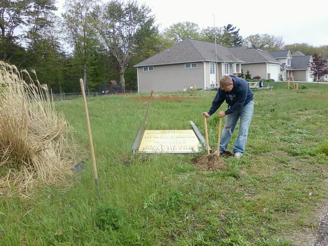 Man installing handicap sign on grassy area near residential neighborhood.