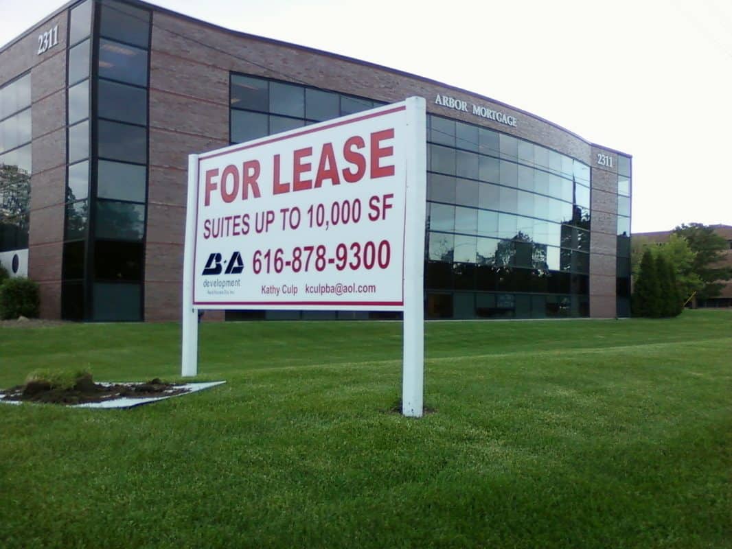 For lease sign on a grassy area in front of a modern office building.