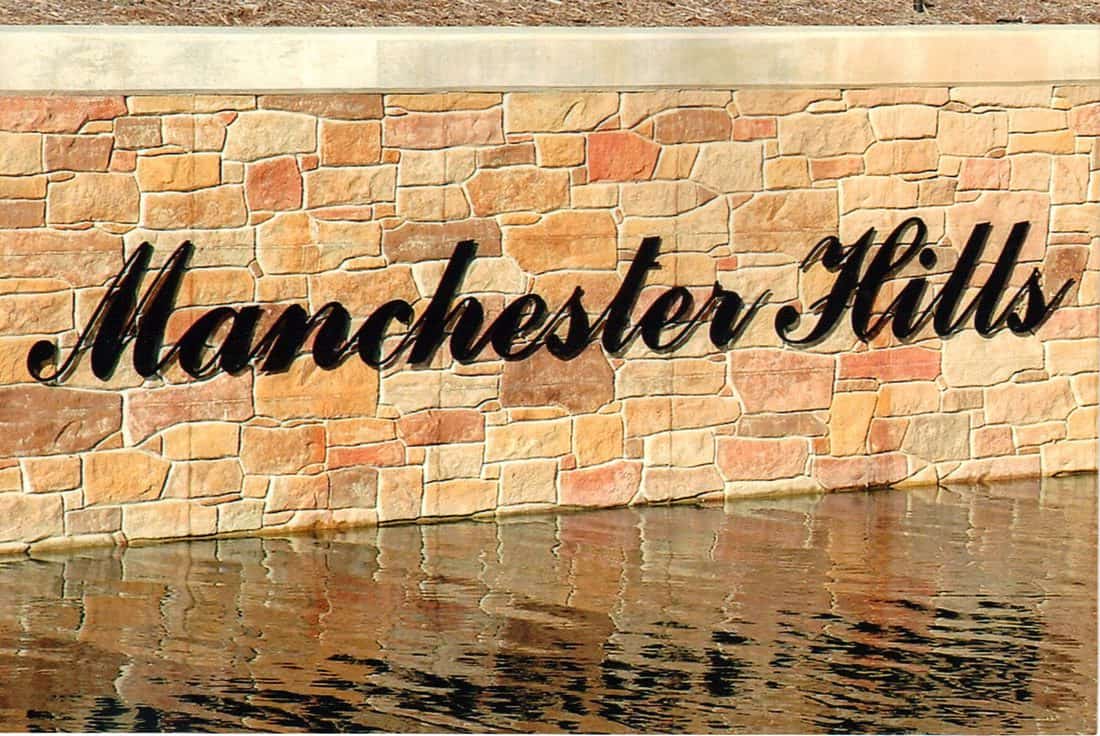 Sign reading Manchester Hills mounted on a brick wall.