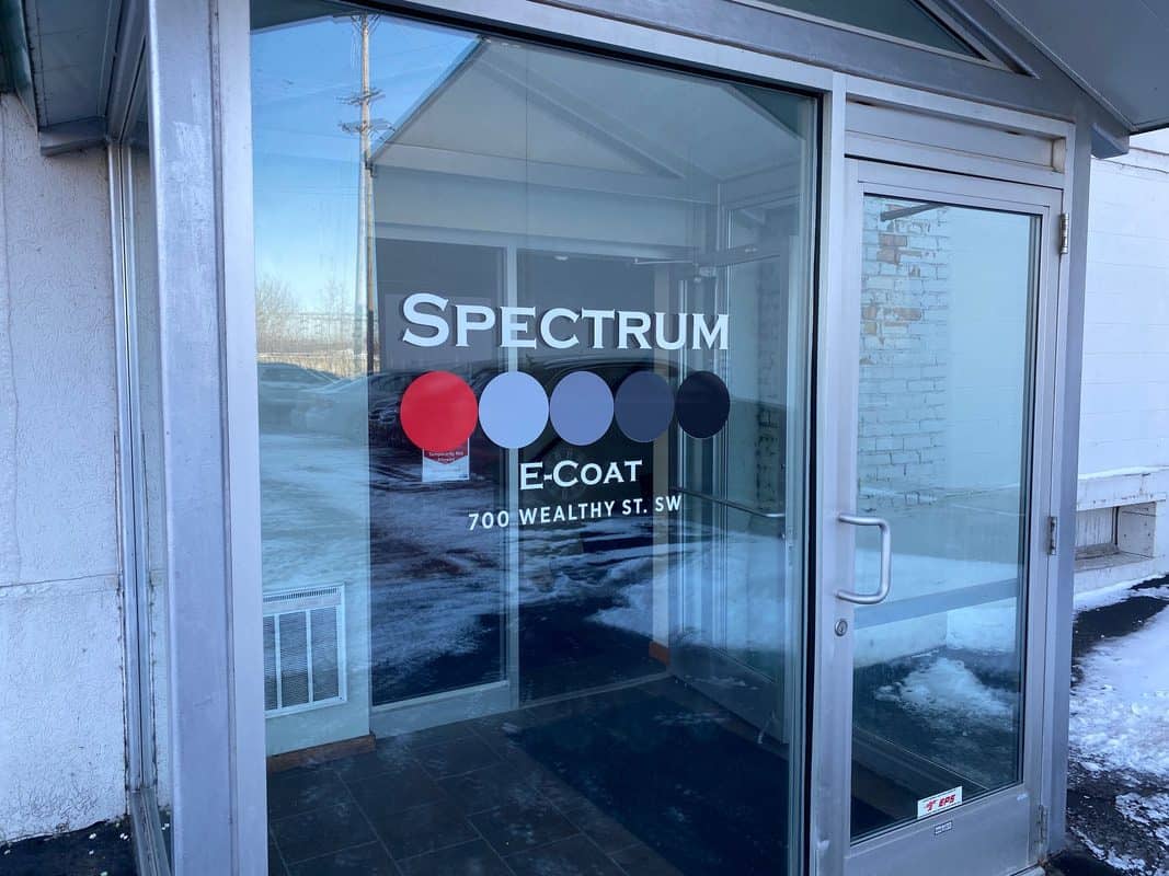 Glass door with Spectrum E-Coat logo and address at 700 Wealthy St. SW.