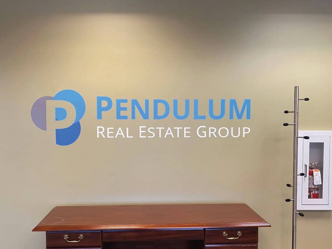 Pendulum Real Estate Group logo on office wall with wooden desk below.