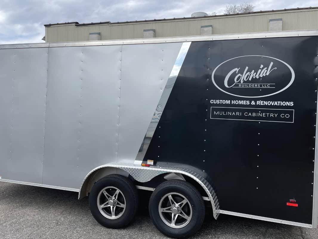 Black and gray trailer with Handicap Sign Inc. logo and custom home renovation ad.