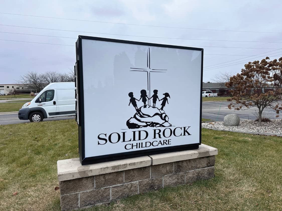 Childcare center sign with children holding hands and a cross above.