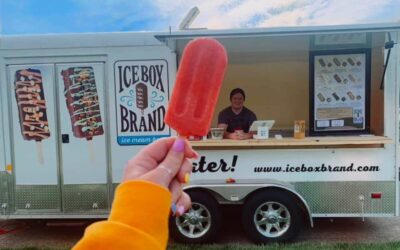 Person holding a red ice cream bar in front of an ice cream truck.