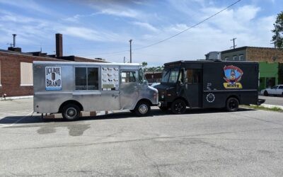 Two ice cream trucks parked on the street with clear sky background.