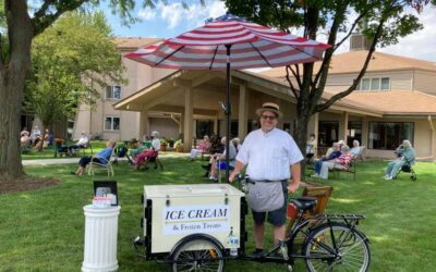 Ice cream cart with umbrella and vendor at park event.