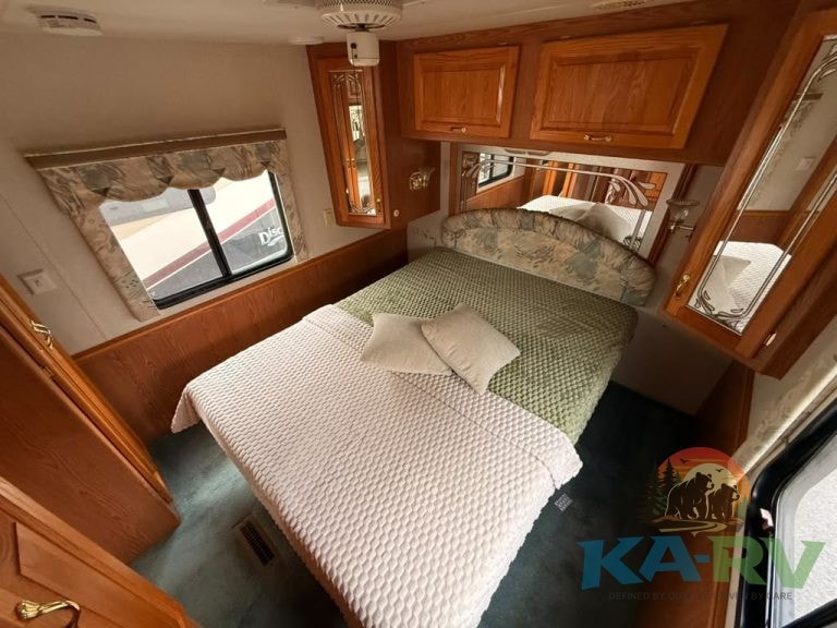 RV bedroom with cozy bed, wooden storage cabinets, and window view.