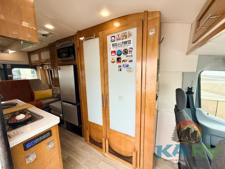 RV kitchen and living space with wooden cabinets and refrigerator.
