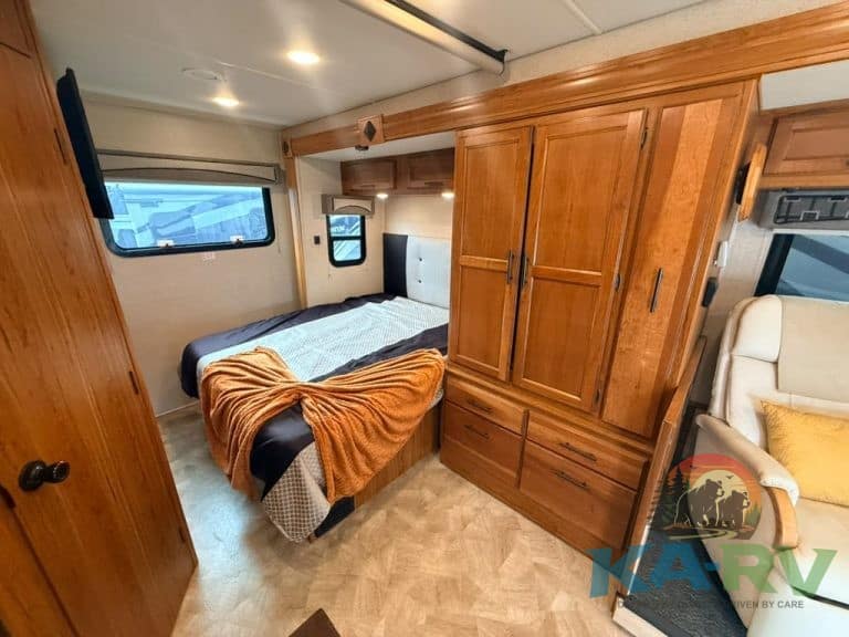 Cozy RV bedroom with wooden cabinets and a large bed with blankets.