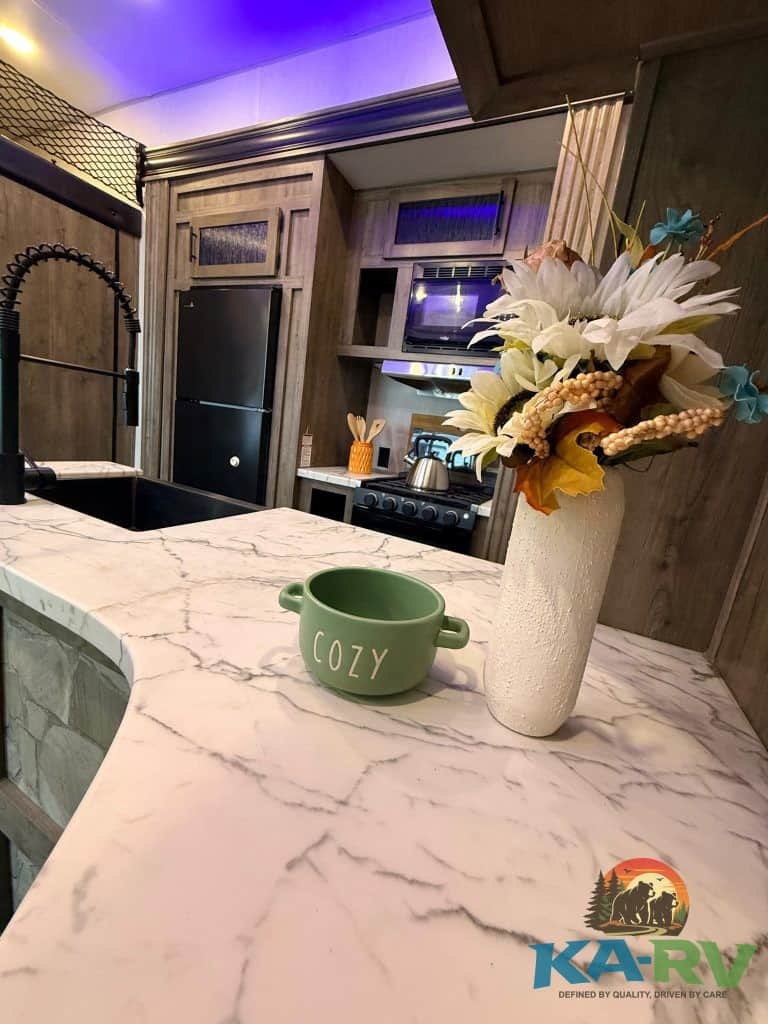 Modern RV kitchen with marble countertop and floral decor.