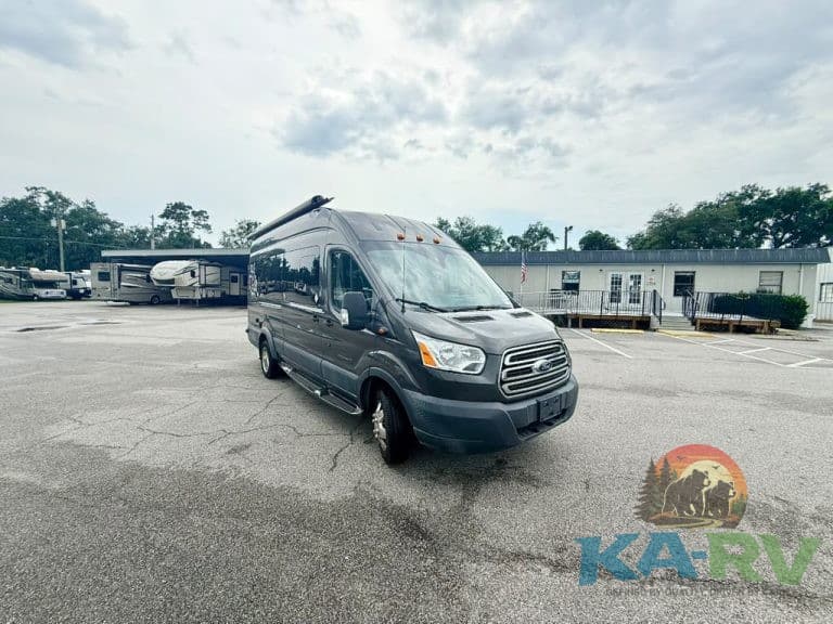 RV repair service van parked in an open lot with trees and buildings in background.