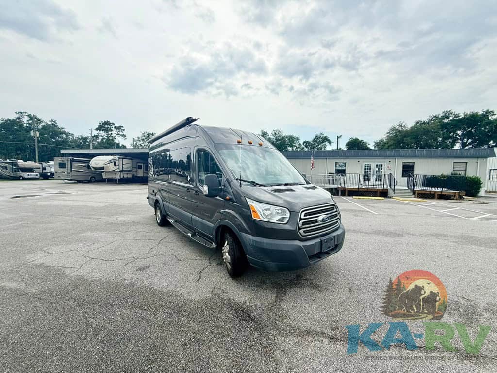 RV repair service van parked in an open lot with trees and buildings in background.