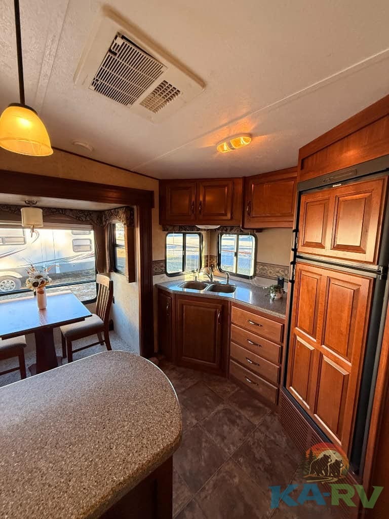 RV kitchen with wooden cabinetry, sink, and windows in a Keystone Cougar 331MKS.