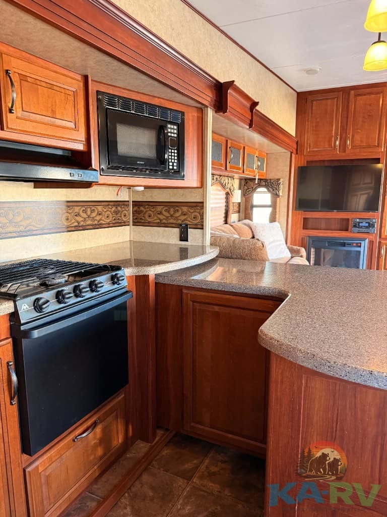 RV kitchen interior featuring wooden cabinetry, microwave, stove, and countertop for optimal cooking.