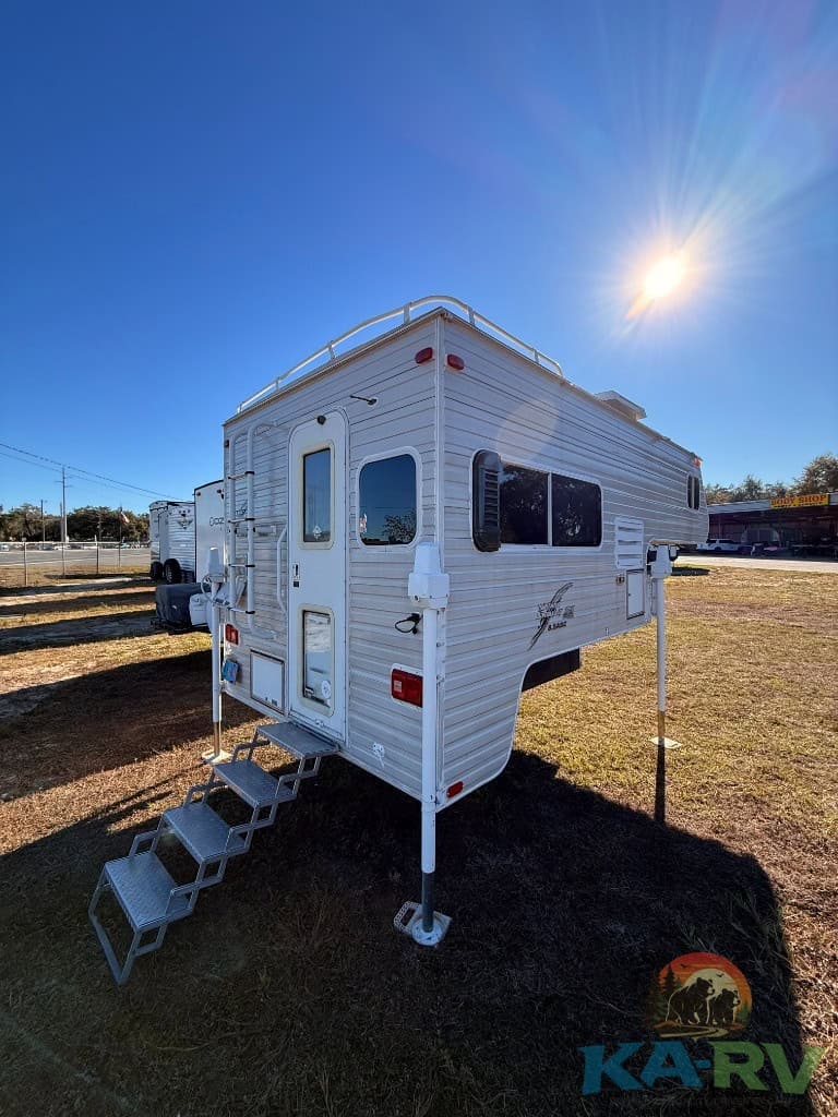 RV trailer with stairs and windows under bright sun.