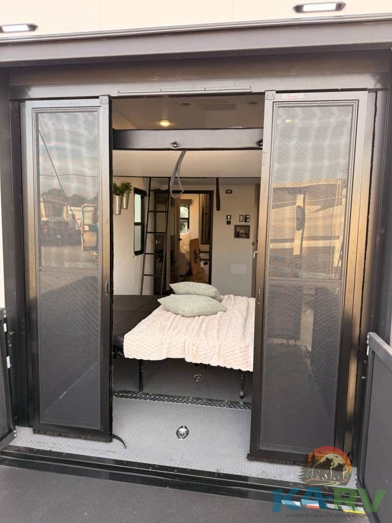 RV bedroom with open sliding doors, showcasing a cozy sleeping area in a Dutchmen Voltage 3800.