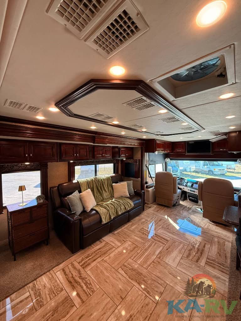 RV interior with leather sofa, wood cabinetry, and panoramic windows for travel comfort.