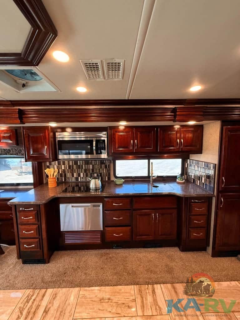 RV kitchen with dark wood cabinets, stainless steel appliances, and tiled backsplash.