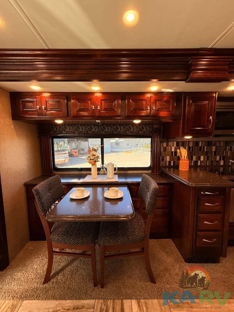 RV kitchen and dining area with wooden cabinets and window view.