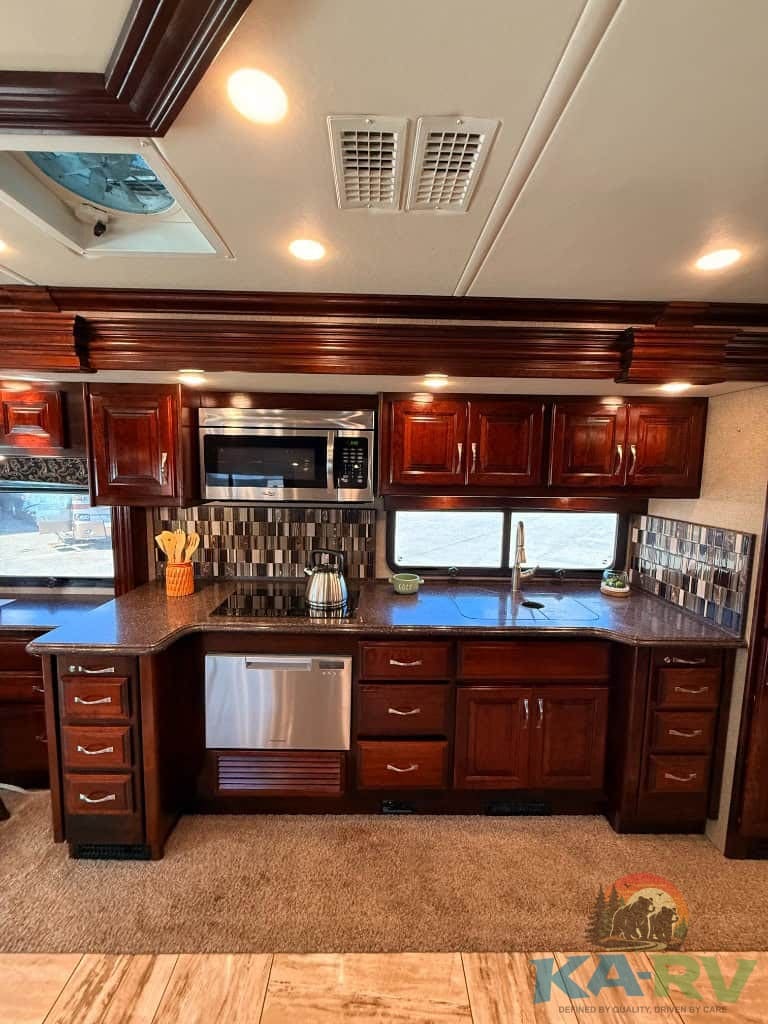 RV kitchen with dark wood cabinets, microwave, and stainless steel appliances.