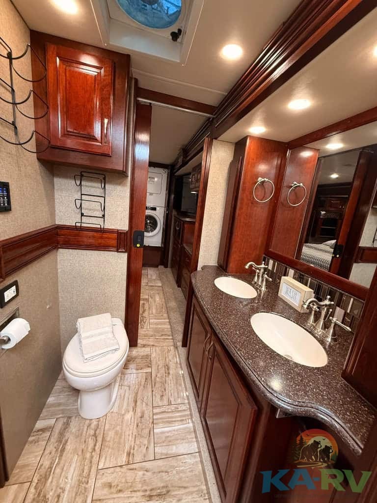 RV bathroom with dual sinks, wood cabinets, and modern fixtures.