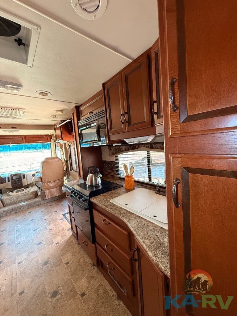 Interior view of a 2013 Four Winds Hurricane RV kitchen with wooden cabinets and modern appliances.
