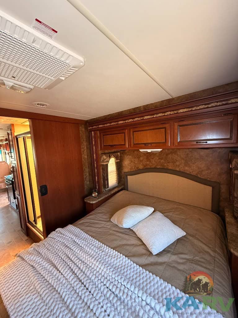 Comfortable RV bedroom with wooden cabinets, bed, and pillows in a 2013 Four Winds Hurricane 29X.
