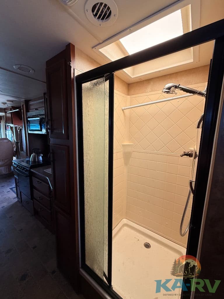 Compact RV shower with beige tiles and skylight.