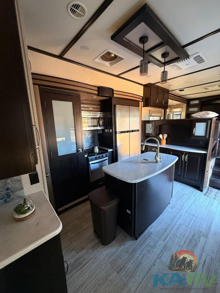 RV kitchen with black cabinets, stainless steel fridge, and island for cooking.