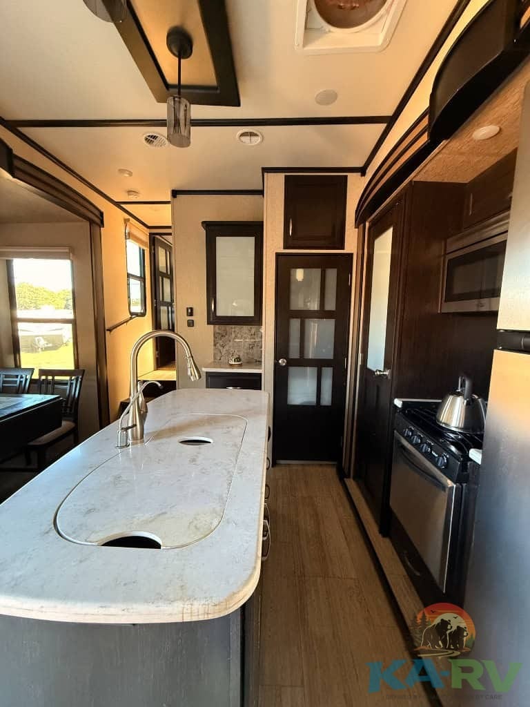 RV kitchen with dark wood cabinetry, marble countertop, and stainless steel appliances.
