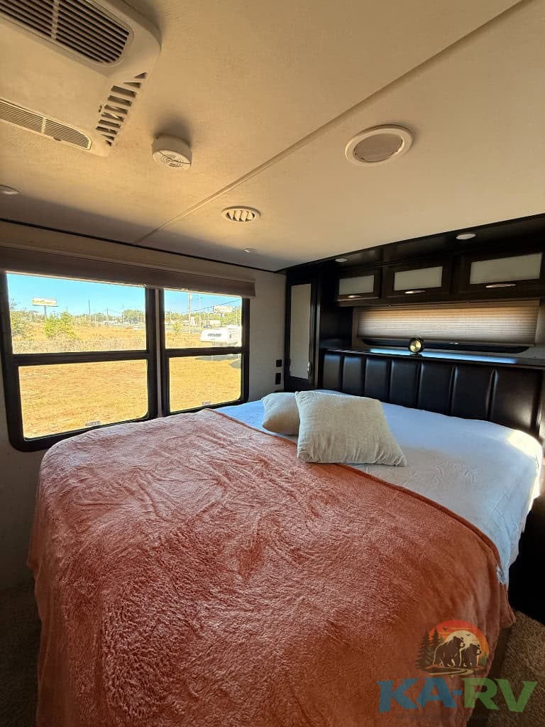 RV bedroom interior with a cozy bed, large windows, and modern design, ideal for comfort during trav.