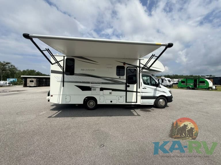 Class C RV with extended awning in a parking lot under cloudy sky.