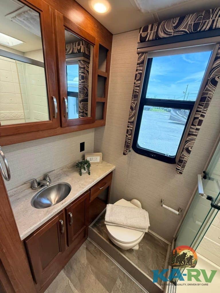 RV bathroom with wooden cabinets, small sink, and window for ventilation.