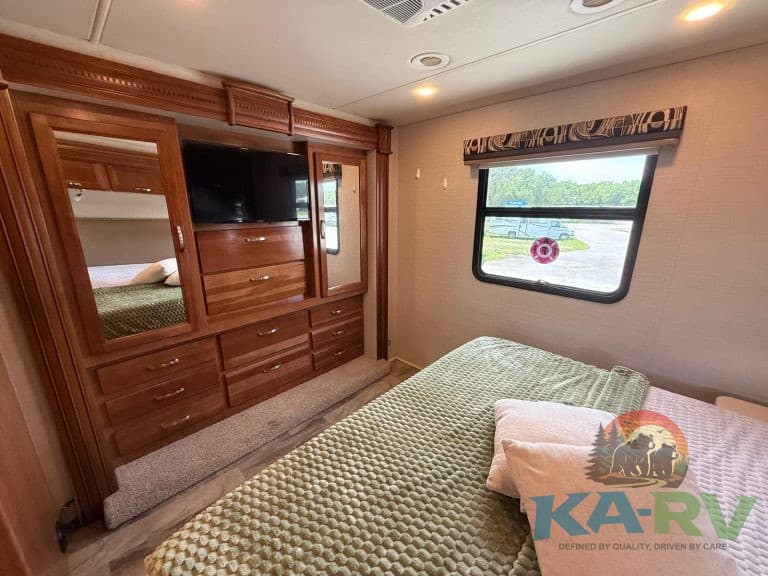 RV bedroom interior with built-in wooden storage, TV, and a large window overlooking the outdoors.