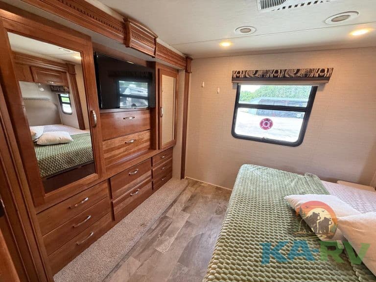 RV interior with wooden cabinets, TV, and a cozy bed. Perfect for comfortable travel and storage in.