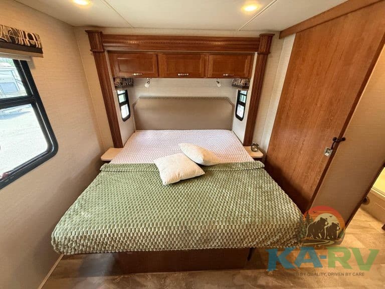 RV bedroom interior with bed, pillows, and wood cabinetry, ideal for travel comfort.