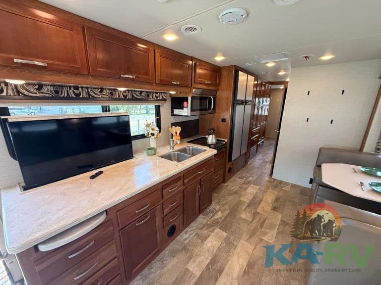RV kitchen interior with wooden cabinets, microwave, and refrigerator in an Optima RV.