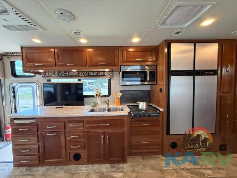 RV kitchen with wooden cabinets, microwave, refrigerator, and stove.