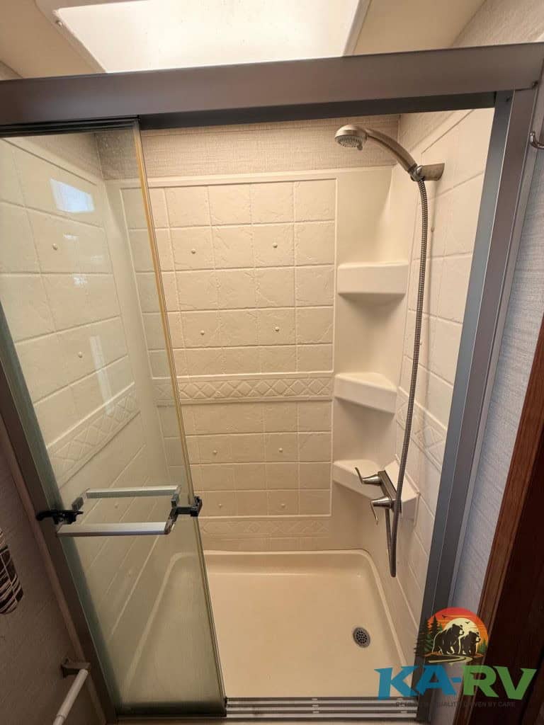 RV shower stall with built-in shelves and handheld showerhead.